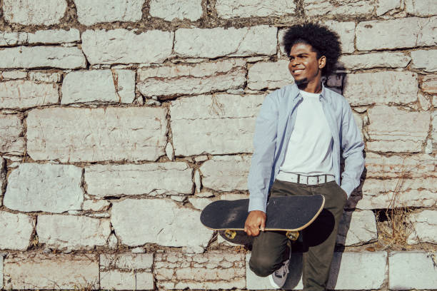 istock Young African American student leaning against a wall with skateboard. Copy space 1349788285