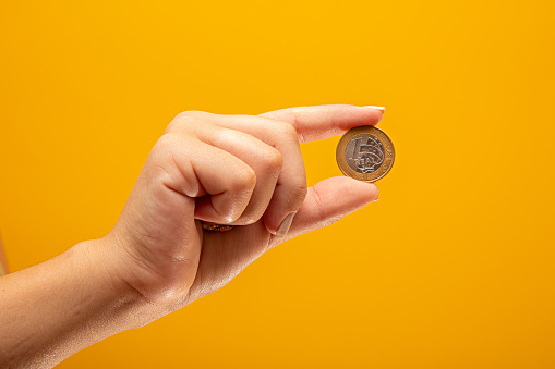 Hand holding one Real coin of Brazil on yellow background. Finance concept.