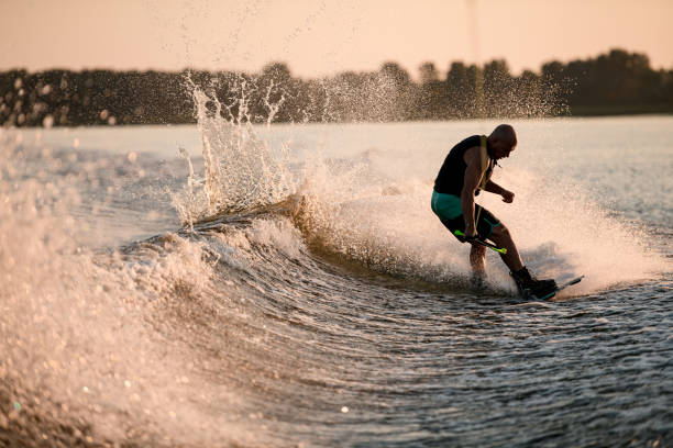 istock Athletic guy holds rope and riding wakeboard on splashing river wave. 1349790181