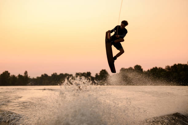 로프에 들고 웨이크 보드에 튀는 파도를 통해 비행 활동적인 남자의 실루엣 - wakeboarding 뉴스 사진 이미지