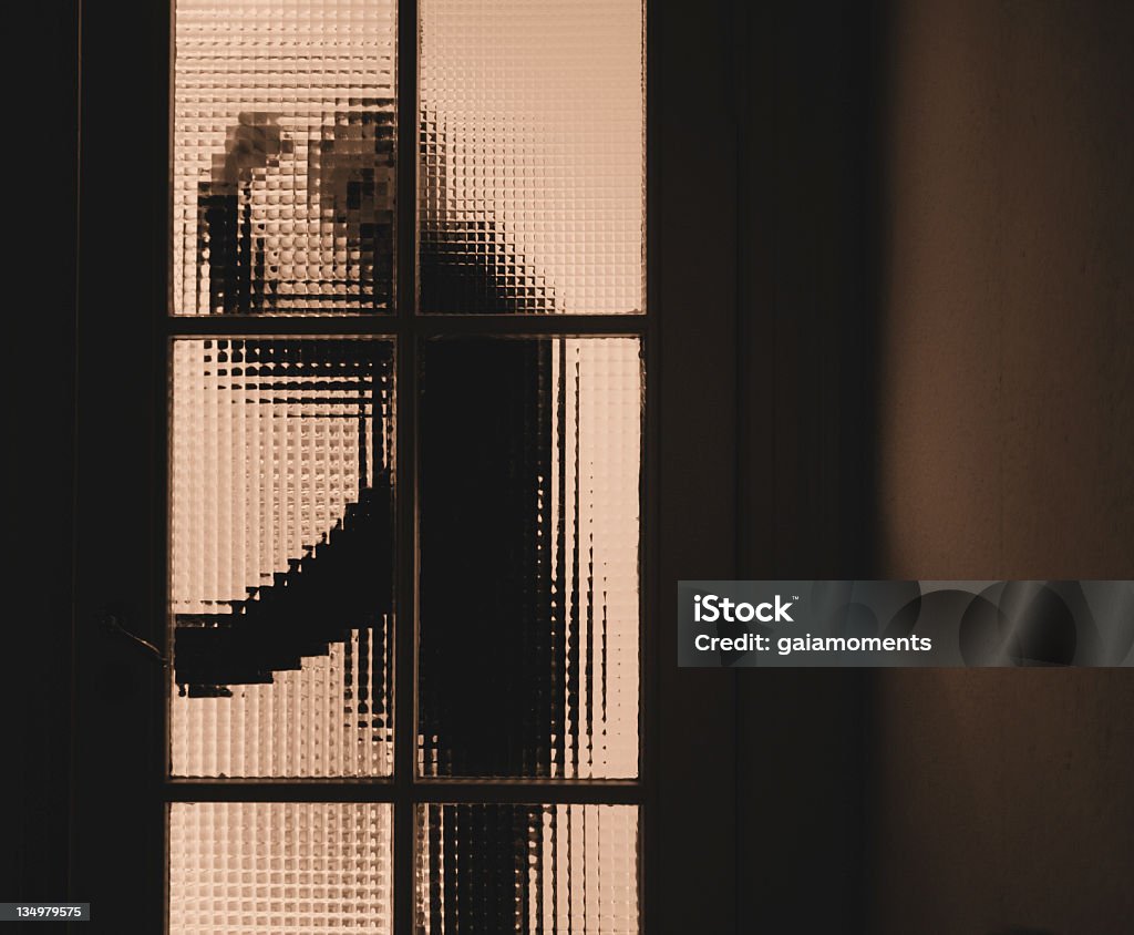 Domestic Violence An aggressive and violent man on his way through a partially transparent glass door (entering a dark room) - with some copy space to the right. Grainy. Sepia. Domestic Violence Stock Photo