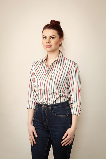 Studio portrait of attractive 25 year old woman with brown hair bun in striped shirt on beige background