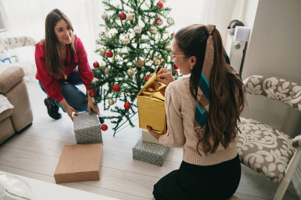 istock Young woman unwrapping a present by a Christmas tree 1349799056