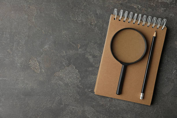 istock Top view of magnifier glass, empty notebook and pencil on grey stone background, space for text. Find keywords concept 1349799190