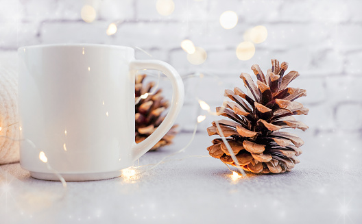White mug and pine cone with christmas lights. Winter holidays