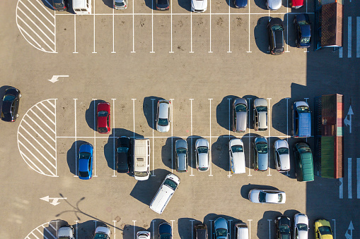 Aerial view of many colorful cars parked on parking lot with lines and markings for parking places and directions.