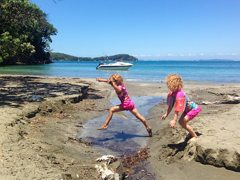 Summer day, children jumping over a stream at the beach, Dairy Bay, Mahurangi Regional Park, Auckland, New Zealand
