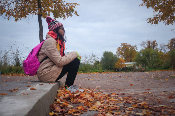 Young attractive blonde girl in orange coat and red beret sending kisses. Sitting on the roof with black ecological zero waste paper made backpack. Positive thinking concept.