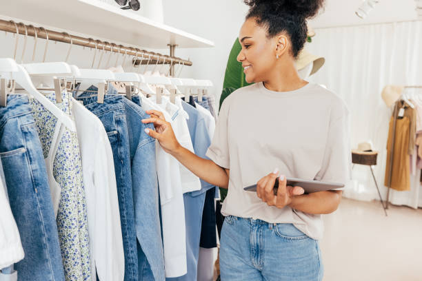 el propietario de una pequeña tienda de ropa que sostiene una tableta digital hace un inventario - shopping clothing store women retail fotografías e imágenes de stock