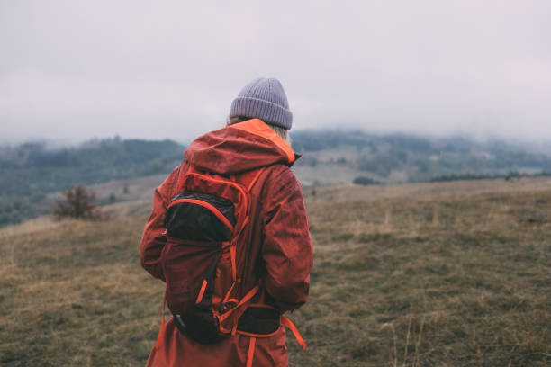 Unrecognizable Female Hiker in a Red Jacket and with a Backpack Exploring the Mountains on a Cloudy Day