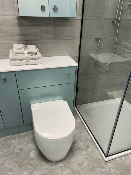 istock Image of modern bathroom with white, toilet with cistern hidden by duck egg blue vanity unit, ribbon tied towel pile, wall cabinet, separate glass panel shower cubicle, natural stone floor tiles 1349823209