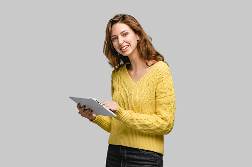 Person using digital tablet for online working. Studio woman portrait of girl wearing yellow sweater. Concept photo with people on gray background and copy space.