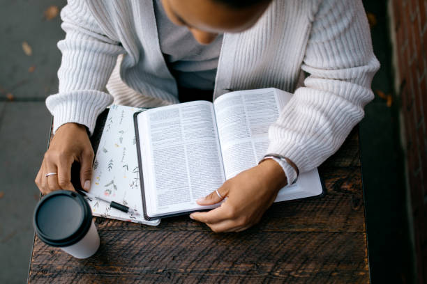 Woman Studying At Outdoor Urban Cafe A mixed race women reads a large Bible / textbook while seated at table outdoors. Could also be a university student on campus. brick cafe stock pictures, royalty-free photos & images