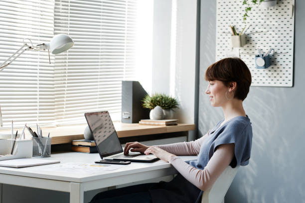 istock Smiling young female strategic manager sitting at desk and browsing internet on laptop while working on project online 1349834119