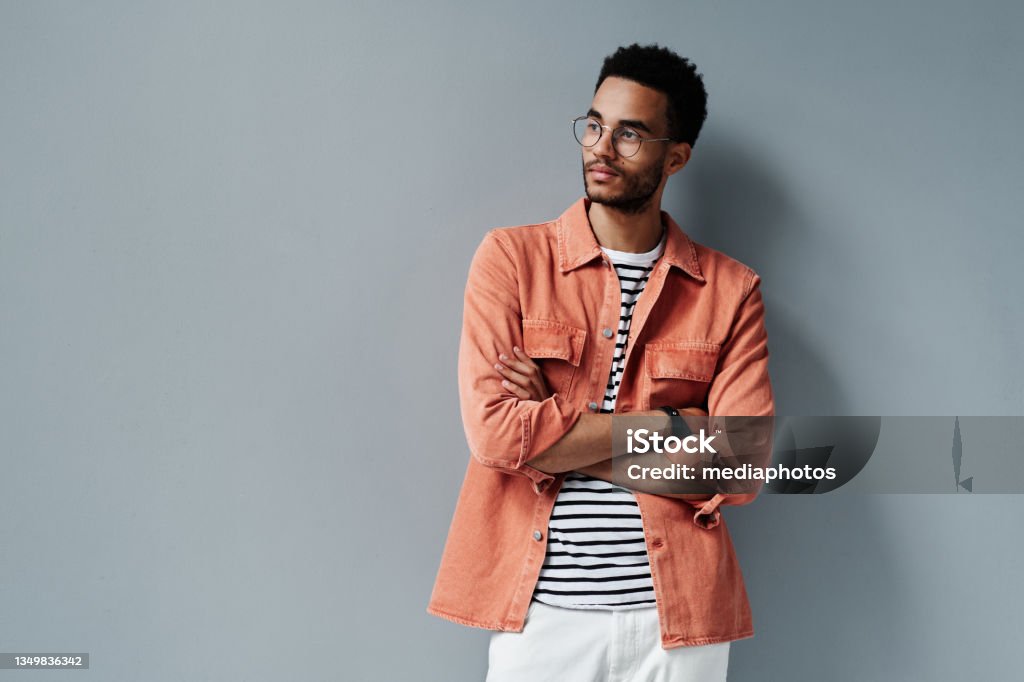 Contemplative young black man with stubble standing with crossed arms against gray wall Contemplative black man Eyeglasses Stock Photo