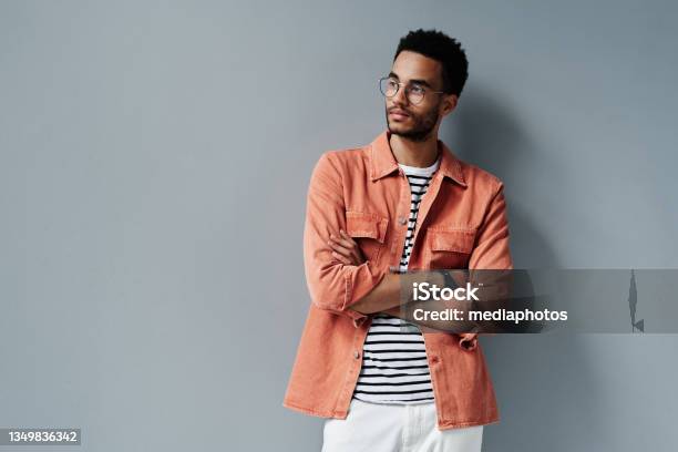 Contemplative Young Black Man With Stubble Standing With Crossed Arms Against Gray Wall Stock Photo - Download Image Now