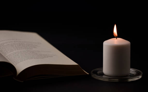 istock candles with flame, and reading book on desk, black background. (focus on candle). 1349837005