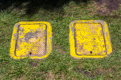 Close-up photo of two yellow water meter covers in the grass.