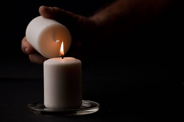 istock burning candle with flame, man's hands lighting candle, black background. (focus on candle). 1349837055