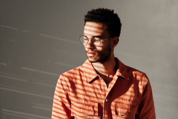 istock Calm young mixed race man in round-shaped glasses standing under light through blinds, isolated background 1349844031
