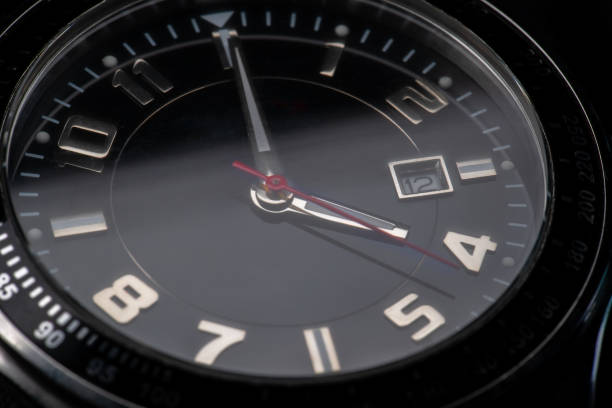 macro shot of a black wrist watch marking 4:00. silver details and red pointer