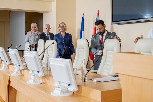 Multiracial colleagues in formal wear smiling and looking away while sitting at table during meeting in modern boardroom