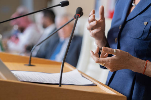 Politician Addressing Conference Close-up of unrecognizable female politician in rings standing at rostrum with microphones and clipboard while addressing conference politics and government stock pictures, royalty-free photos & images