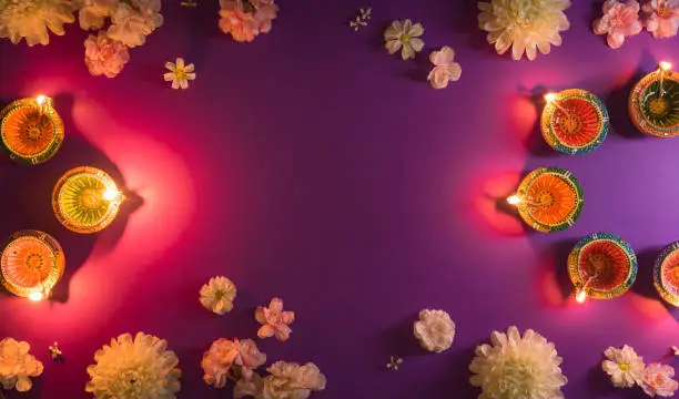 Photo of Happy Diwali - Clay Diya lamps lit during Dipavali, Hindu festival of lights celebration. Colorful traditional oil lamp diya and flowers on purple background