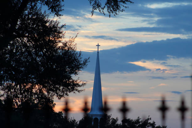 ein kirchturm vor sonnenuntergangshimmel mit einem schmiedeeisernen zaun mit kreuzen oben im vordergrund - city of sunrise sunrise tree sky stock-fotos und bilder