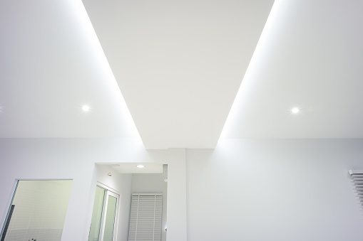 LED strip light and illumination. Also called ribbon light or LED tape. That suspended on ceiling and hide in plasterboard in empty living room include down light, white wall. That is modern luxury interior home building design and technology.