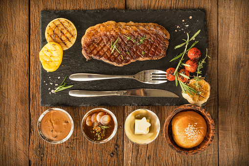 view from top food background of beef picanha steak on stone plate with sauce and bread and butter on wooden table for restaurant menu