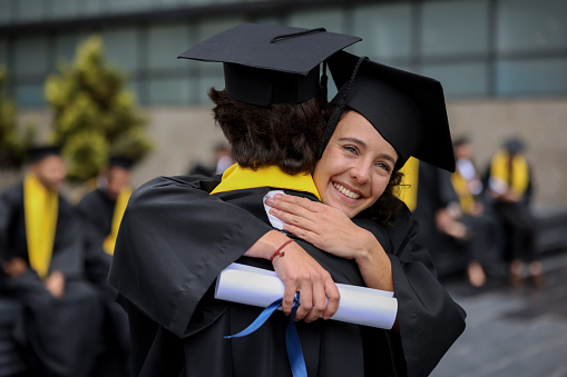 Happy friends hugging after graduating together and smiling while holding their diplomas - graduation day concepts