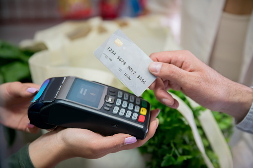 Close up of unrecognizable customer paying for his groceries using a credit card while cashier holds the credit card reader - Technology concepts **DESIGN ON SCREEN AND CREDIT CARD BELONGS TO US**