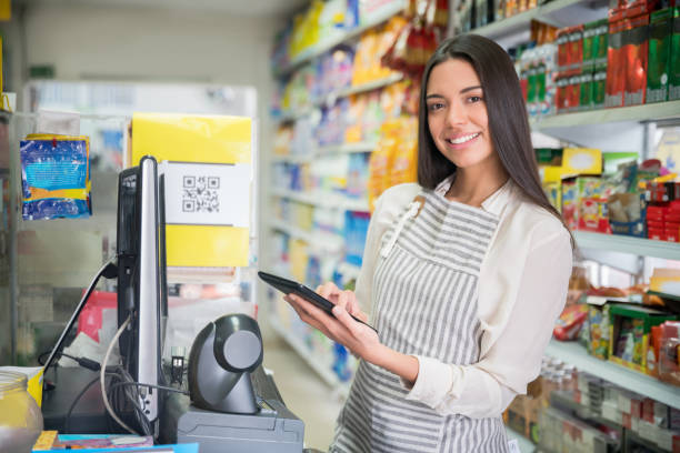 istock Beautiful woman working as a cashier at a convenience store facing camera smiling while holding a tablet 1349881334