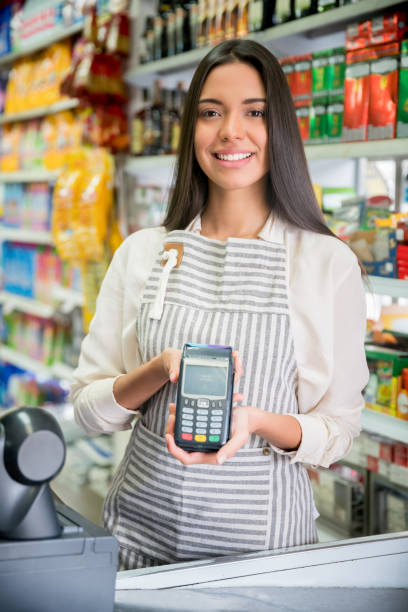 Beautiful cashier at a convenience store holding a credit card reader while smiling at camera