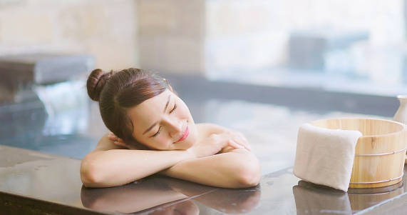 smiling asian young woman lying on the bathtub with crossed arms is relaxing in hot spring