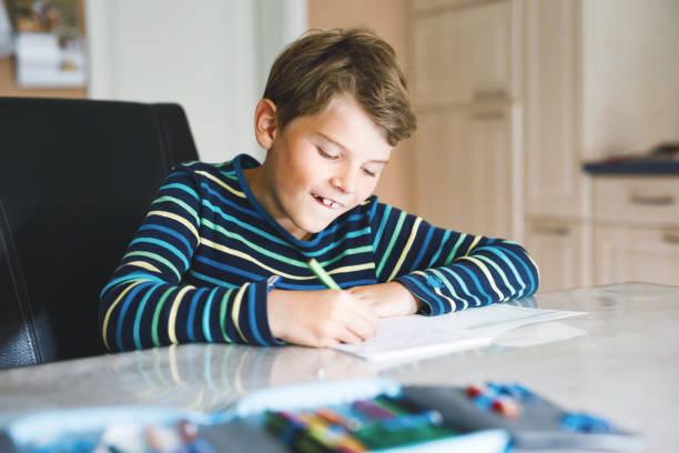 istock Hard-working happy school kid boy making homework during quarantine time from corona pandemic disease. Healthy child writing with pen, staying at home. Homeschooling concept 1349906135