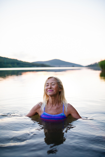 A portrait of active senior woman swimmer diving outdoors in lake.