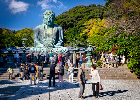 Kamakura, Kanagawa Prefecture, Japan - October 23, 2021: Tourists walk around the Great Buddha, or Kamakura Daibutsu, the 43 foot tall and 103 ton statue which was completed in 1252.