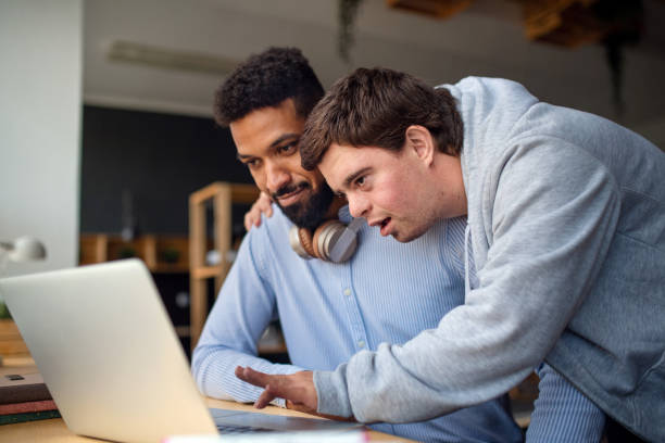 istock Happy young man with Down syndrome and his tutor using lapotp indoors at school. 1349908814