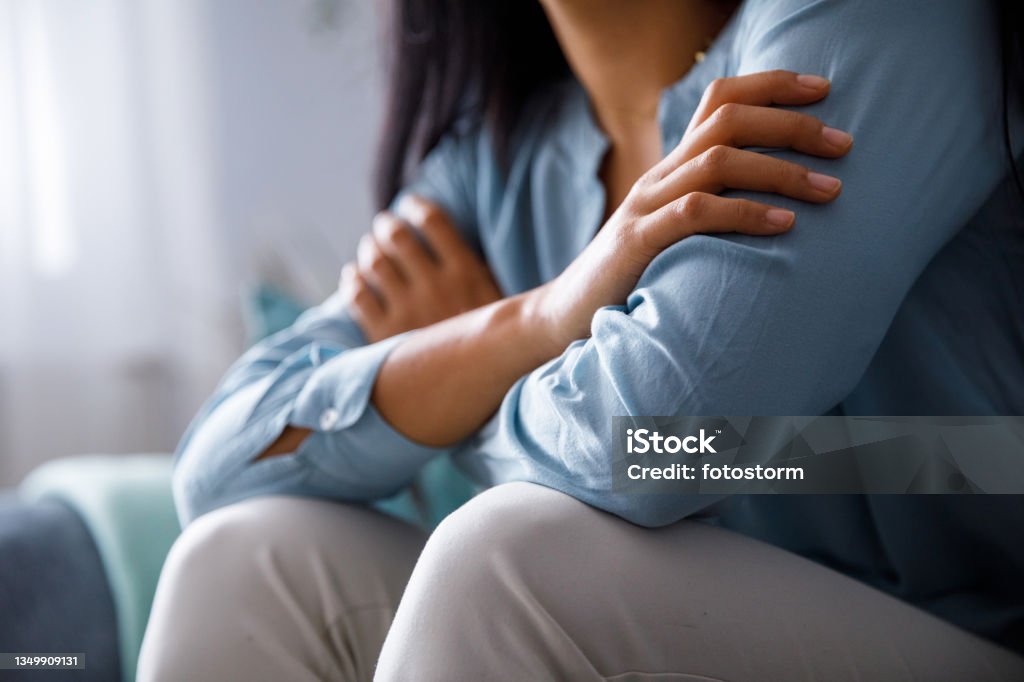 Unrecognizable woman hugging herself to comfort while sad Midsection of unrecognizable young woman hugging herself to comfort while feeling sad and anxious. Loneliness Stock Photo