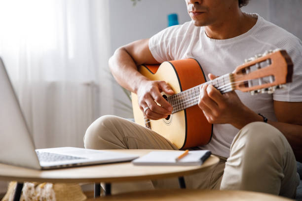 istock Man learning how to play a guitar while watching a video on laptop 1349910816