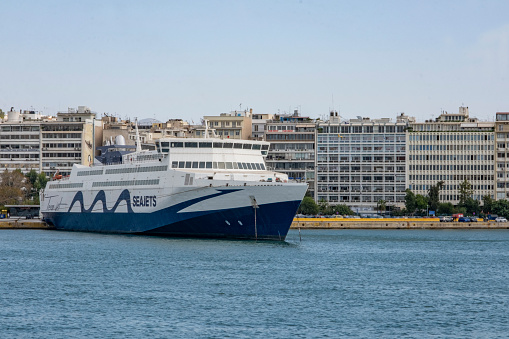 Piraeus, Athens, Greece - September 29, 2021: Transportation concept. Greek ferry series. Side view on SEAJETS ship moored at Piraeus port in front of Buildings. Nautical and city background with copy space