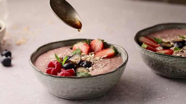 Adding maple syrup in a strawberry smoothie bowl.