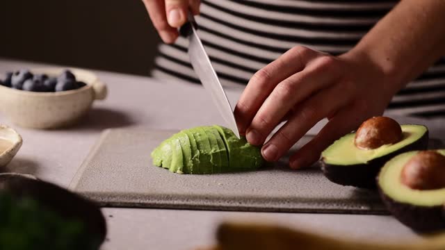 Close-up of a woman cutting avocado on chopping board over kitchen counter