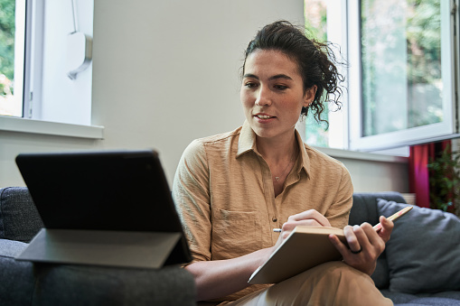 Its fine. Waist up portrait view of the brunette female psychologist making notes with pleasure smile while holding video call with patient