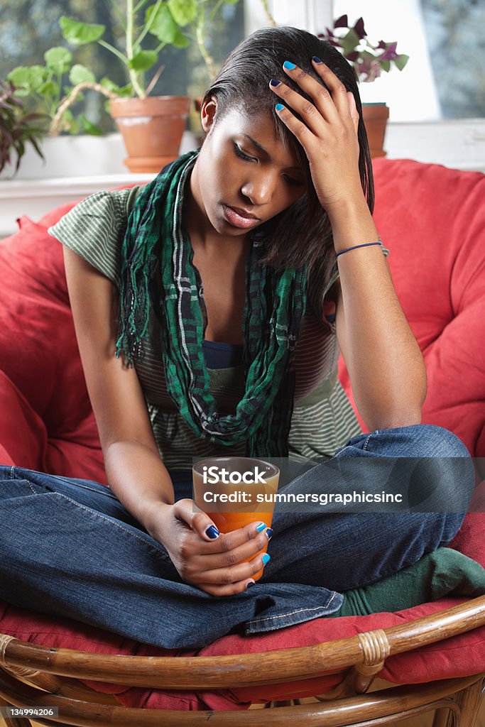 Distraught woman sitting on chair Photo of a sad woman sitting on a chair holding a drink. Adult Stock Photo