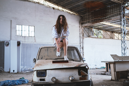 Young woman in abandoned building and standing on a scrap car .