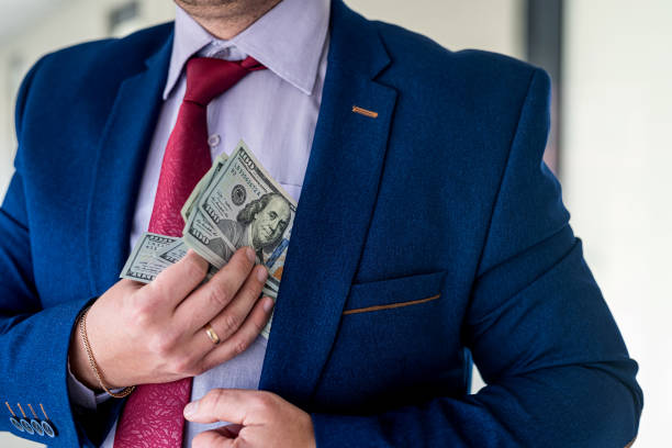 istock Man in blue suit and red tie putting bribe dollar bills into his pocket 1349945554