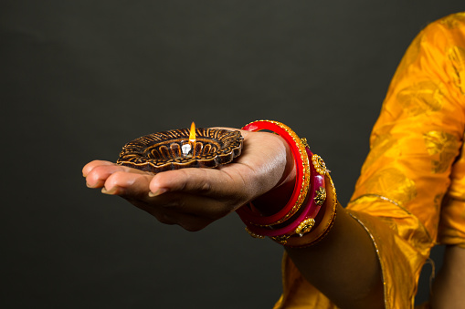 Beautiful Indian Girl holding a diya(terracotta oil lamp). Girl wearing Indian traditional saree and jewellery over gray background. Diwali is biggest festival of India. Diwali is festival of lights.